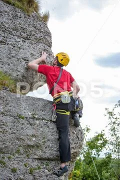 Photo of sportsman in yellow helmet clambering over rock against background of Stock Photos