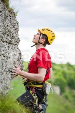 Photo of sportsman in yellow helmet clambering over rock against background of Stock Photos