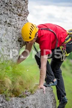 Photo of sporty man looking down in helmet clambering over rock against Stock Photos