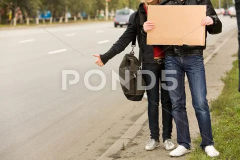 Photo of traveling couple with message board hitchhiking on city road Stock Photos
