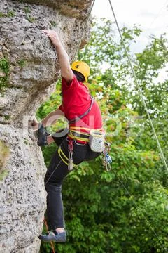 Photo of young sportsman in yellow helmet clambering over rock against Stock Photos