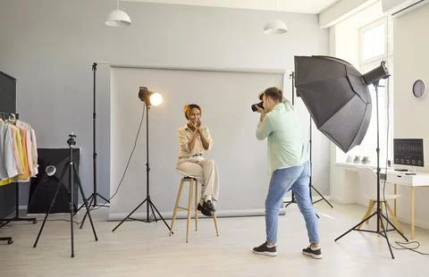 Photographer captures cheerful model on stool in studio using softbox lighting Stock Photos