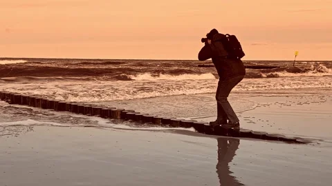 Photographer Capturing Ocean Waves at Sunset on Serene Coastal Landscape 库存影片 297539341