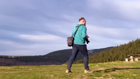 Photographer carrying camera equipment while hiking in mountain terrain Stock Footage 346769543