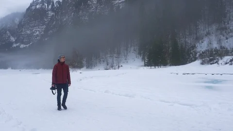 Photographer exploring snow covered path around frozen lake Stock Footage 102527406