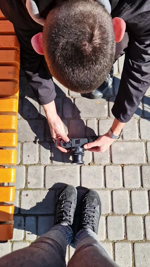 Photographer Holding Mirrorless Camera Taking Photo of Shoes on Pavement Stock Footage 339002748