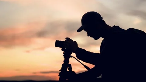 Photographer man with backpack uses camera with tripod against amazing beautiful Stock Footage 296180032