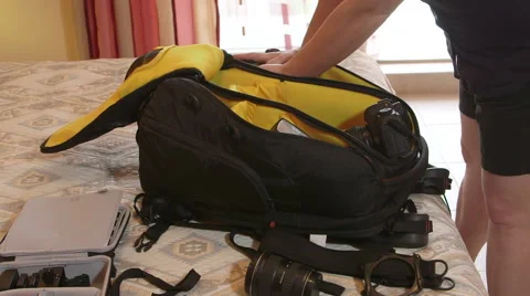 Photographer packing photo camera backpack on bed in hotel room Stock Footage