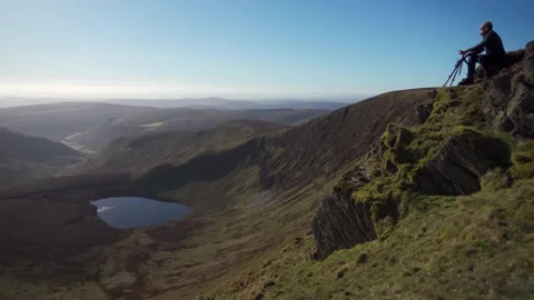 A photographer setting up a camera on the edge of a cliff in the Welsh mountains 動画素材 242047423