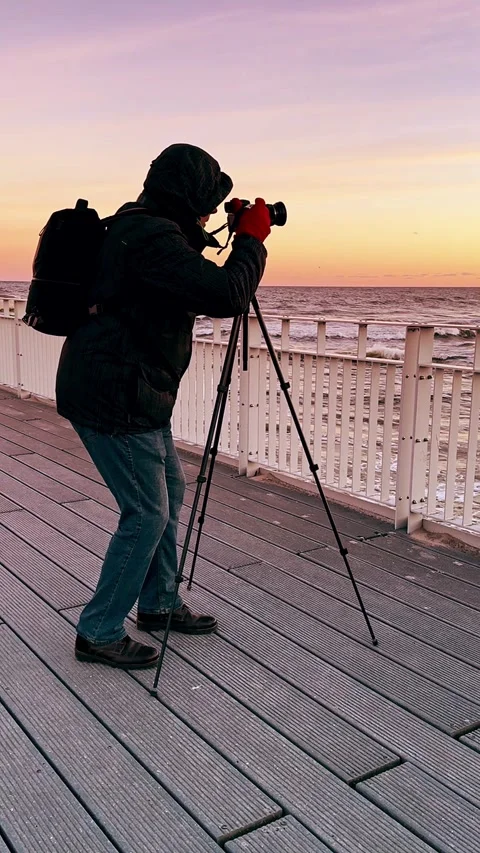 Photographer Setting Up Camera on Pier at Sunset Over Ocean Horizon Stock Footage 297616734