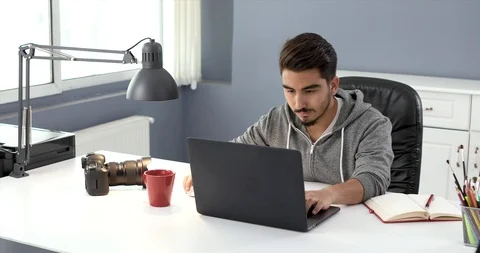 Photographer sitting on table at studio and sharing his photos to social media Stock Footage 107741080