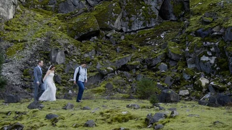Photographer walks in front of rocky cliff with Bride and Groom Stock Footage