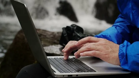 Photographer working on a computer on a waterfall background. Stock Footage 78661774