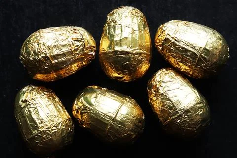 Photography of six chocolate easter eggs wrapped in gold foil on slate back.. Stock Photos