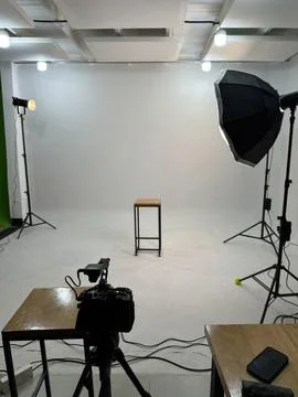 Photography studio setup with lights, camera and stool on white backdrop Stock-Fotos