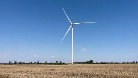 Photorealistic image of a single white wind turbine standing tall in a harvested Stock Footage 338389006