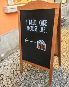 Phrase "I need cake because life" on advertising black board on the street. Stock Photos