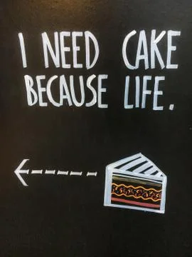 Phrase "I need cake because life" on advertising black board on the street. Stock Photos