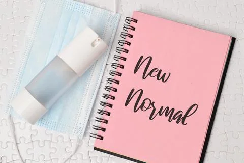 Phrase NEW NORMAL written on notebook with hand sanitizer and face mask. Stock Photos