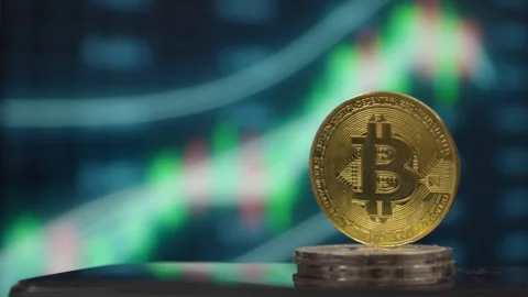A physical Bitcoin coin displayed against a blurry cryptocurrency chart Stock Footage 334771325