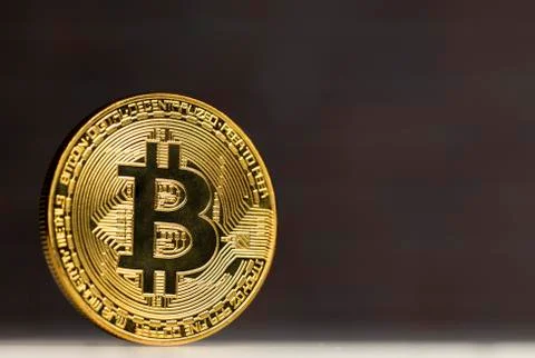 Physical bitcoin standing at a white table in front of a brick wall Stock Photos