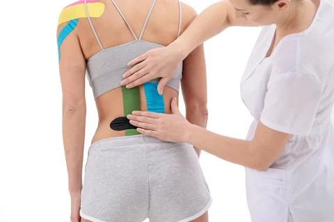 Physical therapist applying kinesio tape on female patient's lower back Stock Photos