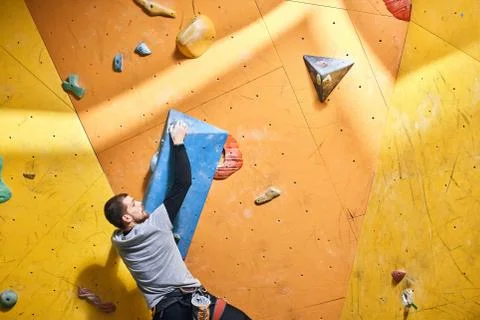 Physically challenged boulderer hanging on large blue artificial rock hold Stock Photos
