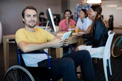 Physically disabled man on wheelchair using tablet in office Stock Photos