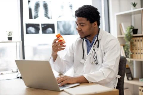 Physician holding pill bottle while surfing internet indoors Stock Photos