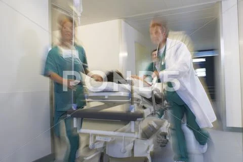 Physicians Moving Patient On Gurney Through Hospital Corridor Stock Photos