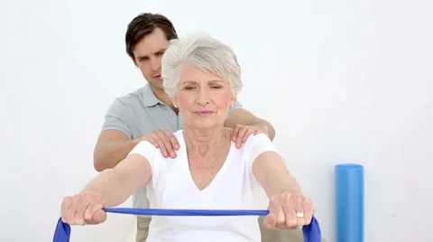 Physiotherapist checking senior patients shoulder alignment with resistance band Stock Footage 34666052