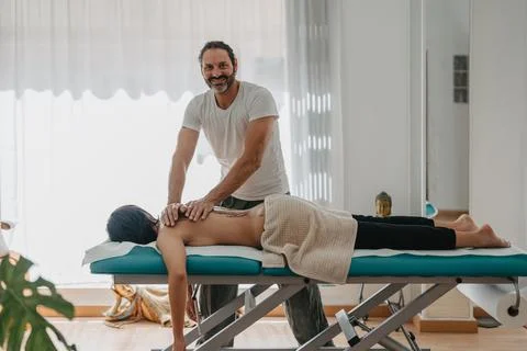 Physiotherapist smiling on camera while massaging a young patient Stock Photos