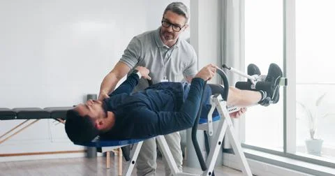 Physiotherapy, consulting and inversion table with man in clinic for back pain Stock Photos