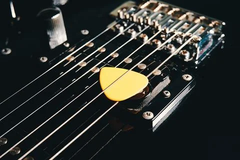 Pick between the strings on the soundboard of a black electric guitar close-up Stock Photos
