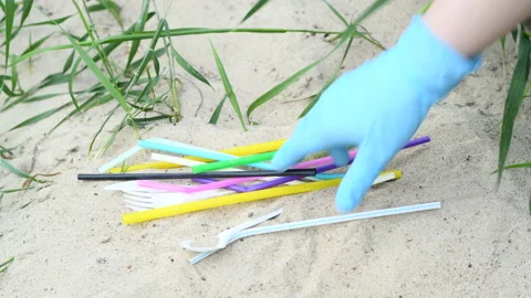 Picking up drinking straws and plastic cutlery from sand Stock Footage 136437134