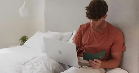 Picking up green passport, man verifying info on silver laptop for accuracy in Stock Footage 316478677