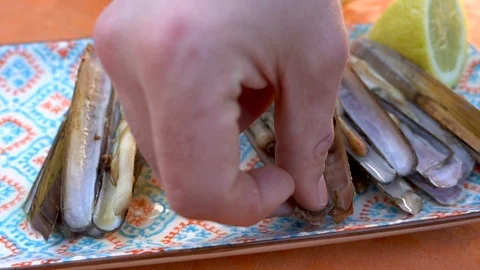 Picking up the grooved razor shell by hand from the plate to eat Stock Footage 126001966