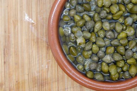 Pickled capers resting in brine inside terracotta bowl Stock Photos