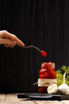 Pickled cherry tomatoes in a jar, one tomato on a vintage fork over a jar, .. Stock Photos