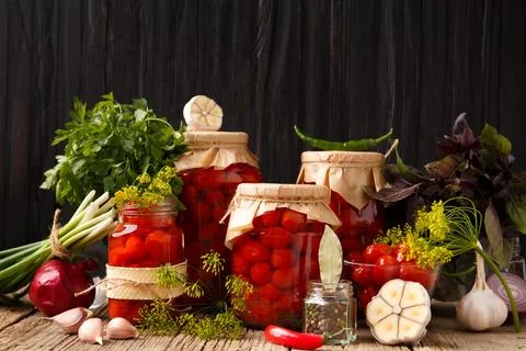 Pickled cherry tomatoes in jars and spices on a wooden background Stock Photos