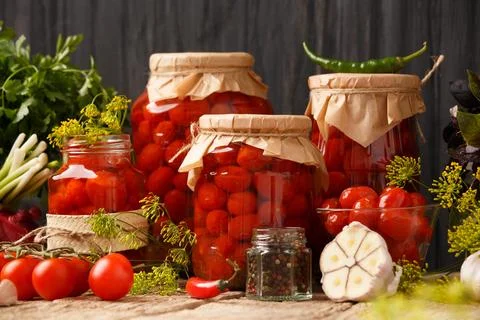 Pickled cherry tomatoes in jars and spices on a wooden background Stock Photos