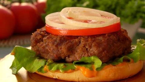 Pickled cucumber slices fall on onion rings on the half-prepared cheeseburger Stock Footage 127643074