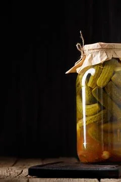 Pickled cucumbers in a jar on a dark background with place for text close-up. Stock Photos