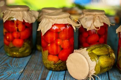 Pickled tomatoes and cucumbers in glass jars on an old wooden table. Stock Photos
