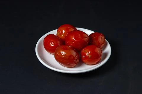 Pickled tomatoes on a black background. Pickled tomatoes on a white plate on a d Stock Photos