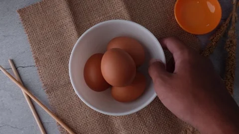 Picks up and puts down a white bowl containing pile of eggs on straw mat Stock Footage 272563693