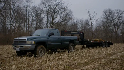 Pickup truck with flat bed trailer hitched to it sits in a corn field in Stock Footage 123778411