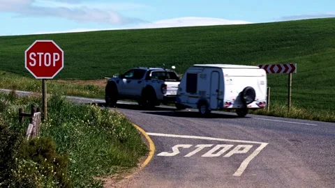 A pickup truck pulling a trailer drives past a stop sign on a tar road with Stock Footage 343460661