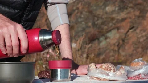 Picnic in nature. Standing at the table, man pours tea from thermos into cup. 4K Stock Footage 167580798