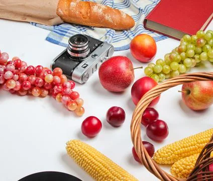 Picnic setting with camera, basket, fruit, baguette on white background. Retr Stock Photos